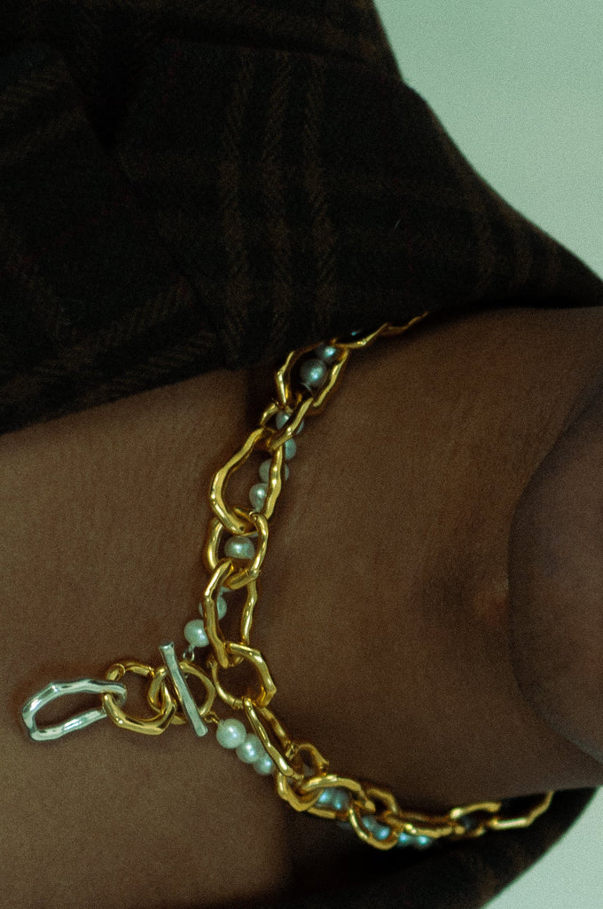 Gold chain bracelet with pearls on a person's wrist against a neutral background