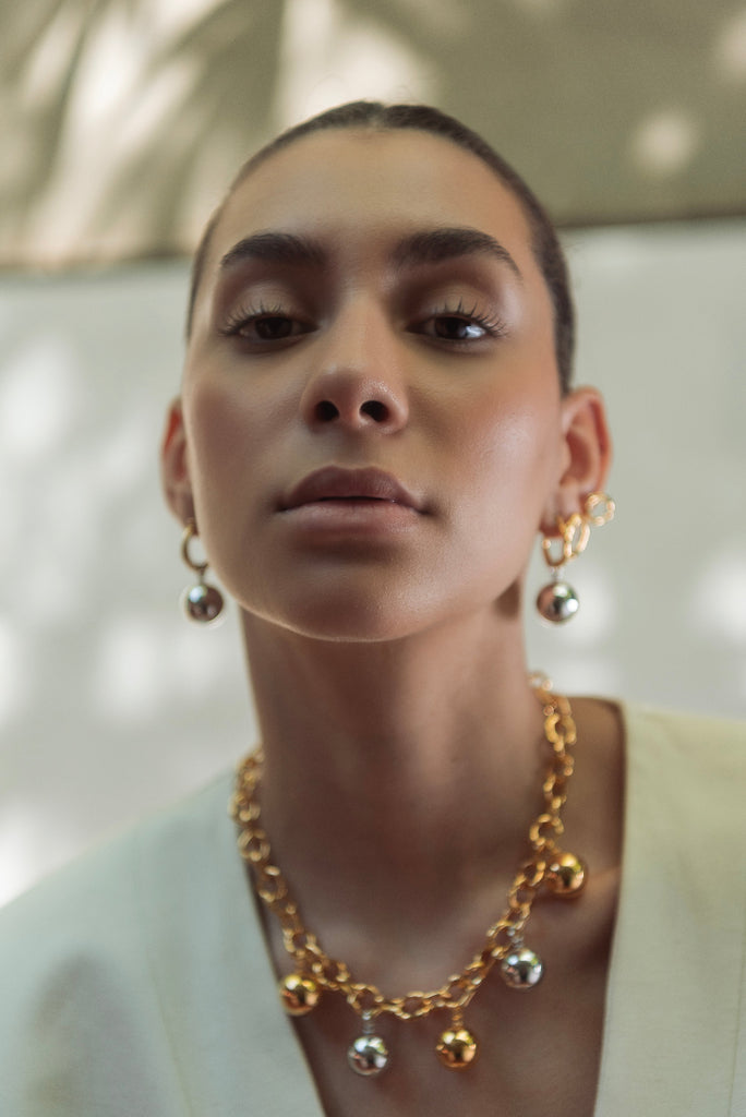 Woman wearing a gold chain necklace with spherical pendants against a blurred natural background