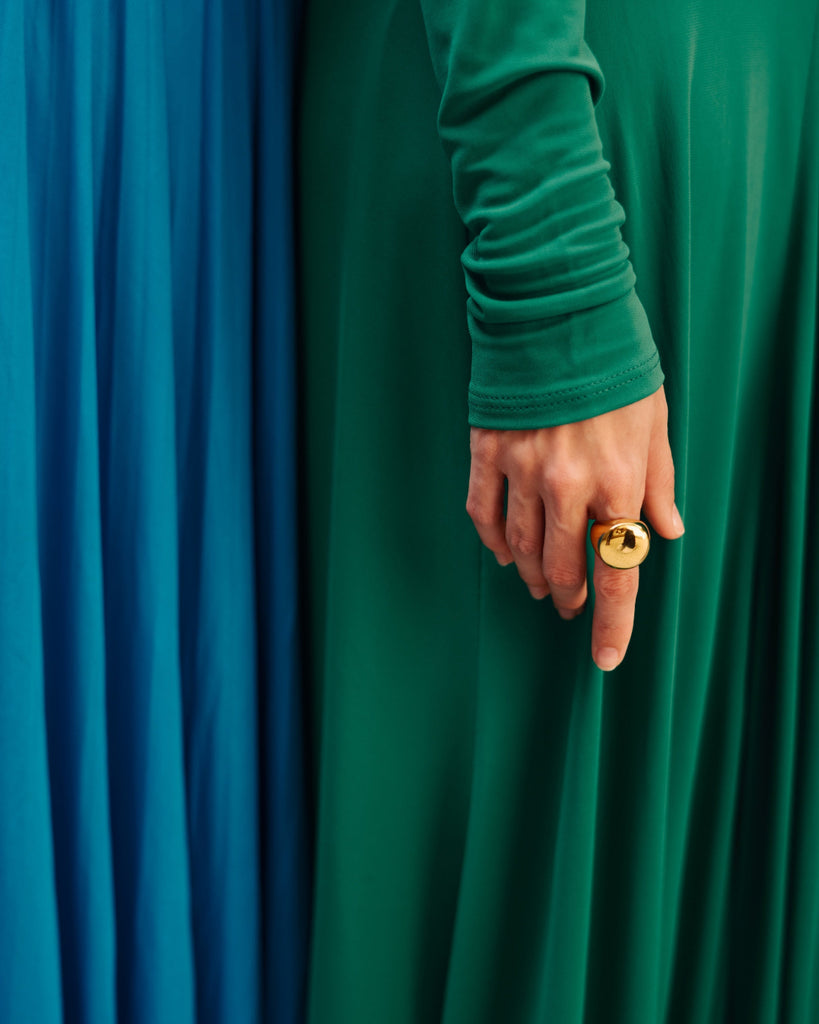 Person wearing a green long-sleeve shirt with a gold ring against a green and blue curtain background