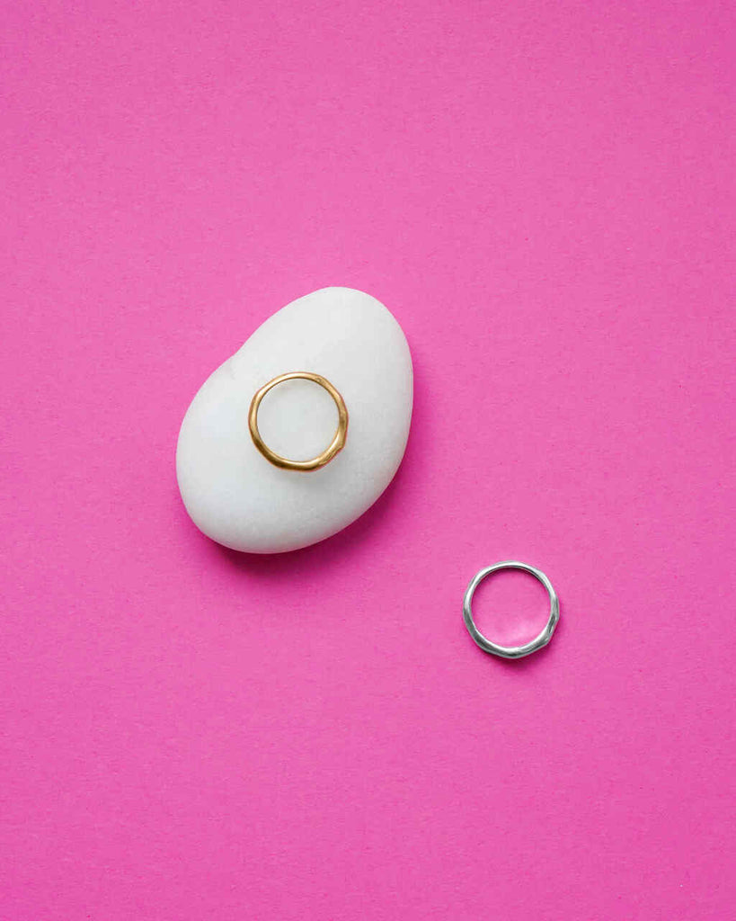 Gold and silver rings on a white stone against a pink background
