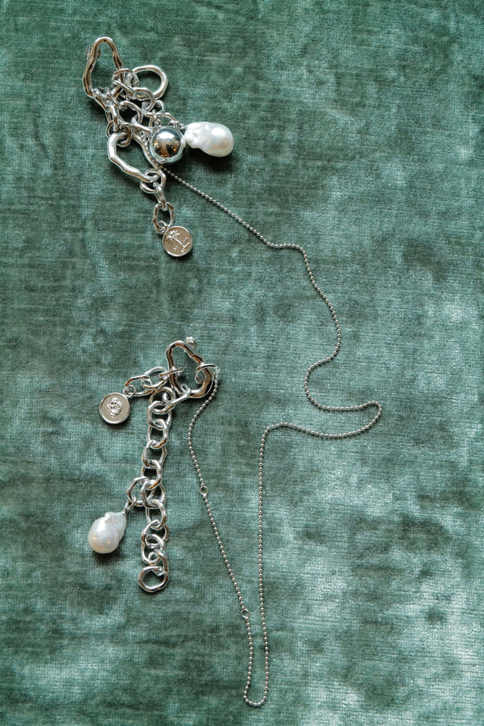 Bespoke Silver brooch with charms on a textured green surface for the Met Gala 