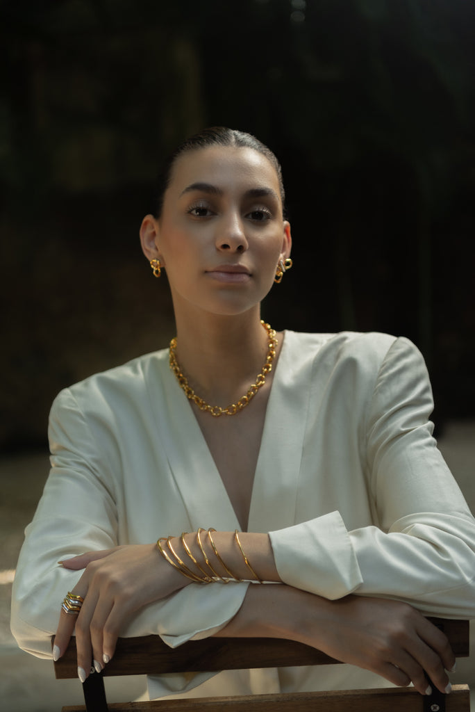 Woman wearing gold jewelry sitting on a chair with a blurred background