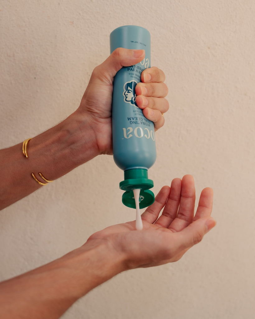 Hand holding a blue and green bottle dispensing soap into another hand against a beige background