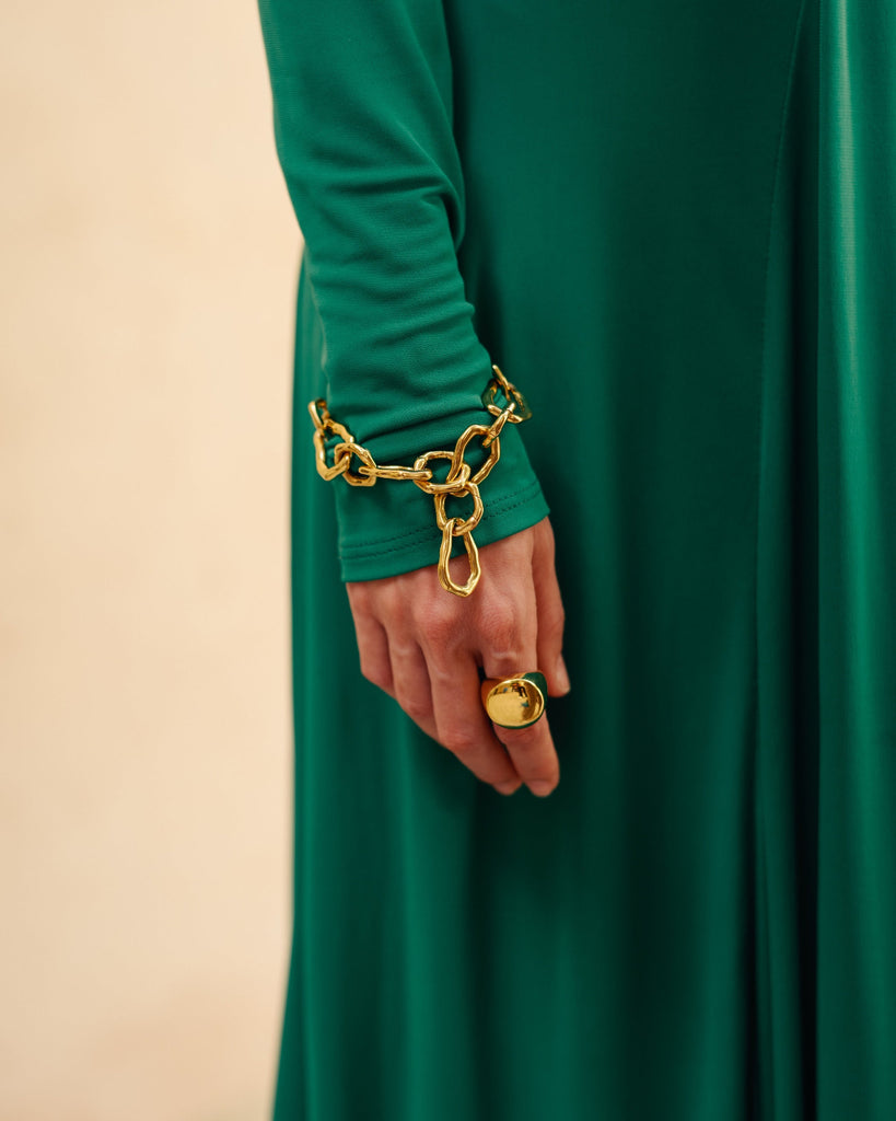 Person wearing a gold chain bracelet and ring wearing a green dress
